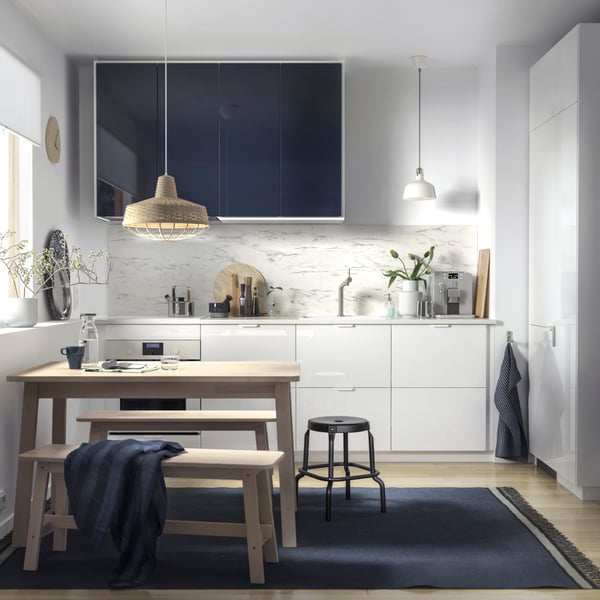 Immagine di una cucina con mobili bianchi METOD e pensili blu laccati. Di fronte, un tavolo e una panca in legno con uno sgabello in metallo.