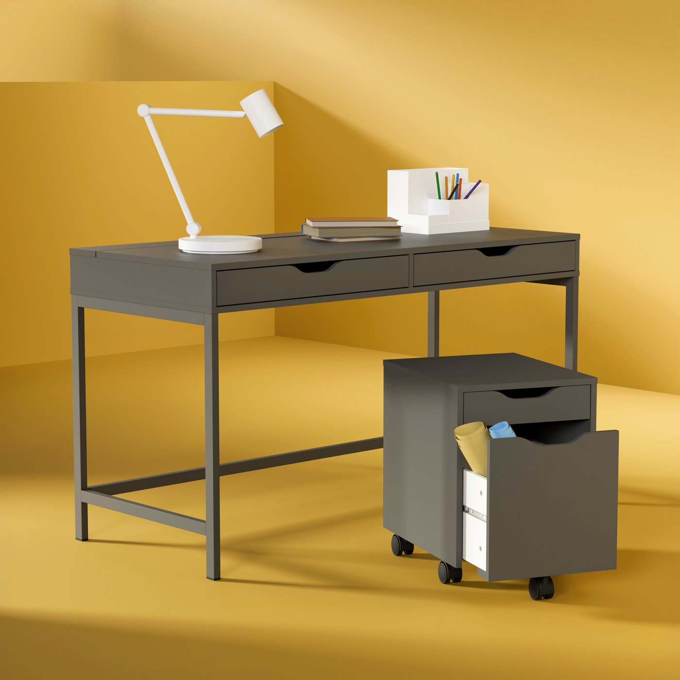 Tummanharmaa ALEX-työpöytä ja ALEX-laatikosto keltaista taustaa vasten.