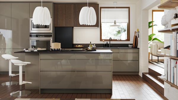A straight kitchen with fronts in VOXTORP high-gloss dark grey-brown and SINARP brown has a dining table in front of it.