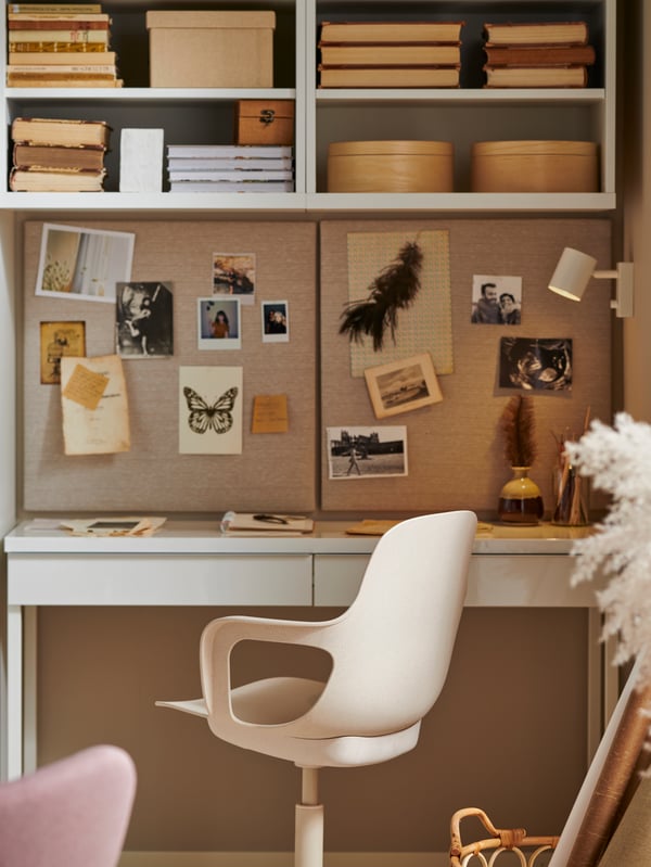 A workspace with a high-gloss white BESTÅ BURS desk, a swivel chair, two memo boards with pins, books, boxes and photos.