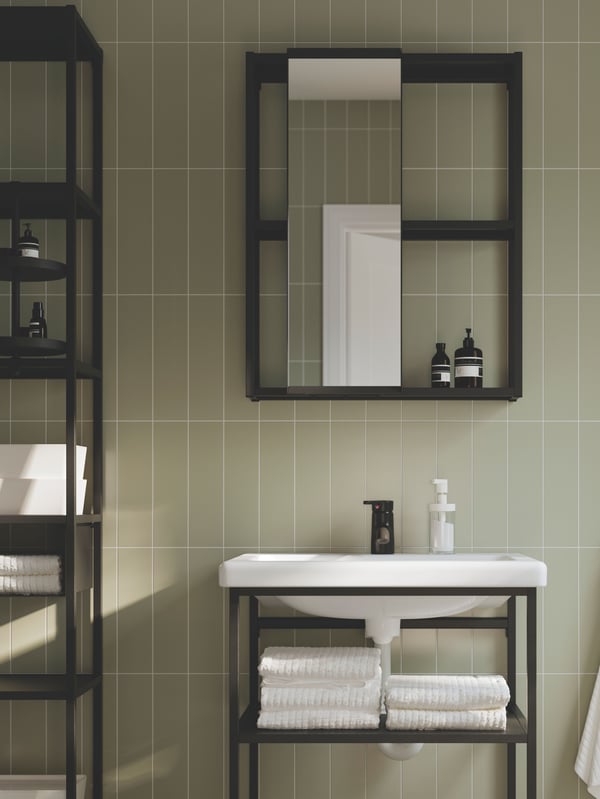 An ENHET bathroom in anthracite with open shelves and a cabinet with a mirror door is placed against a grey-green wall.