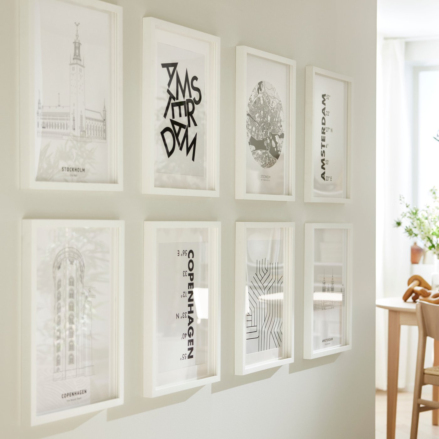 Eight BILD posters in white RÖDALM frames hang on a white wall above next to a dining area group in light wood.