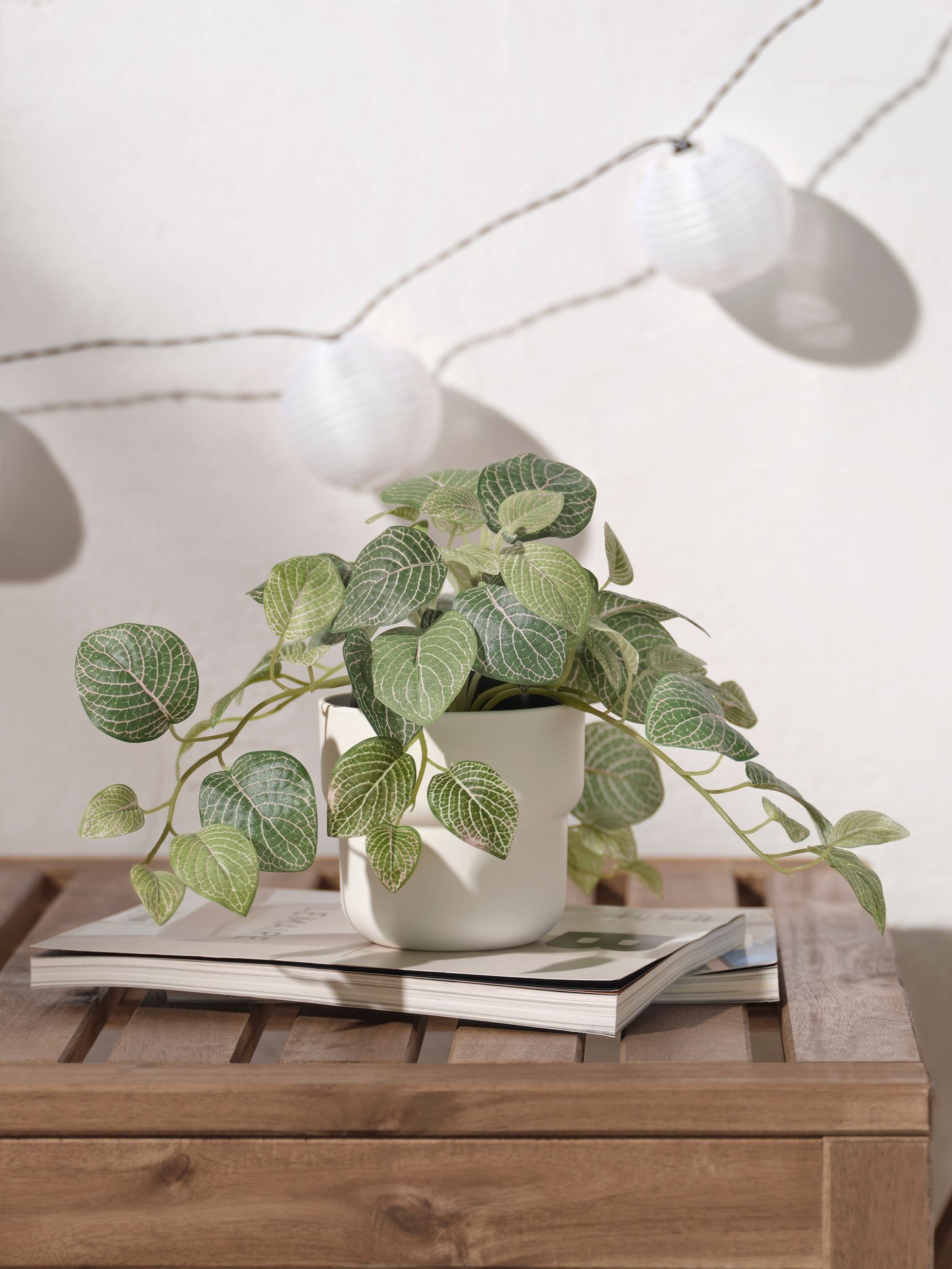 Una planta arficial FEJKA encima de un libro en una mesa de madera.