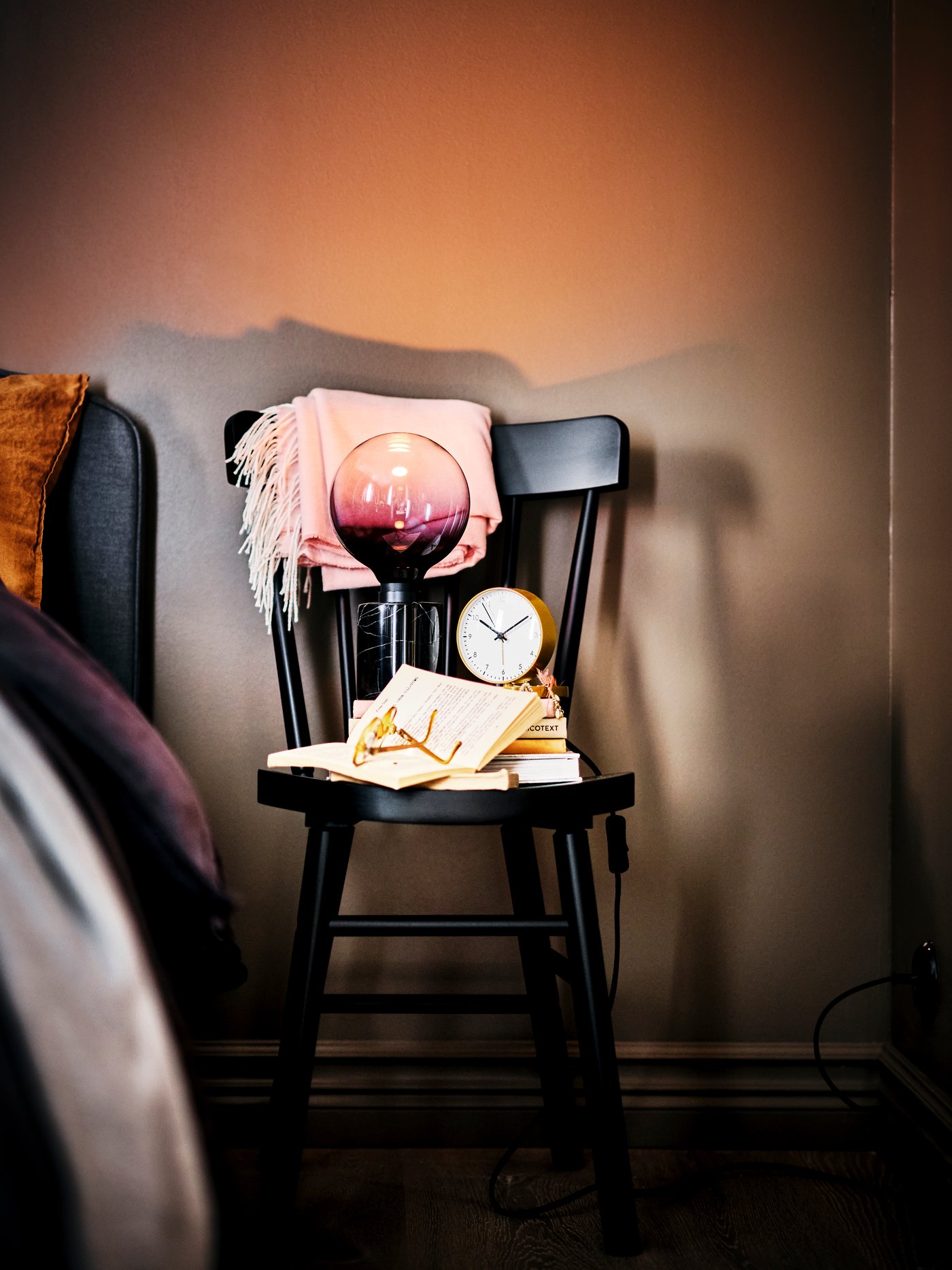 A black marble MARKFROST table lamp atop a black NORRARYD chair next to a grey HAUGA upholstered bed with storage.