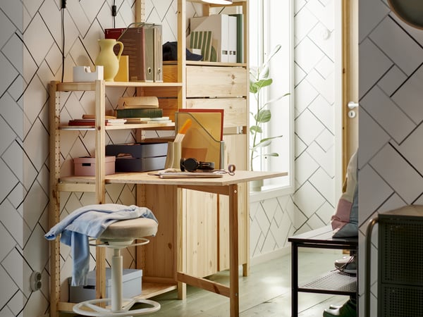Fold-out table and shelving unit in light wood in corner of home with plant in the background.