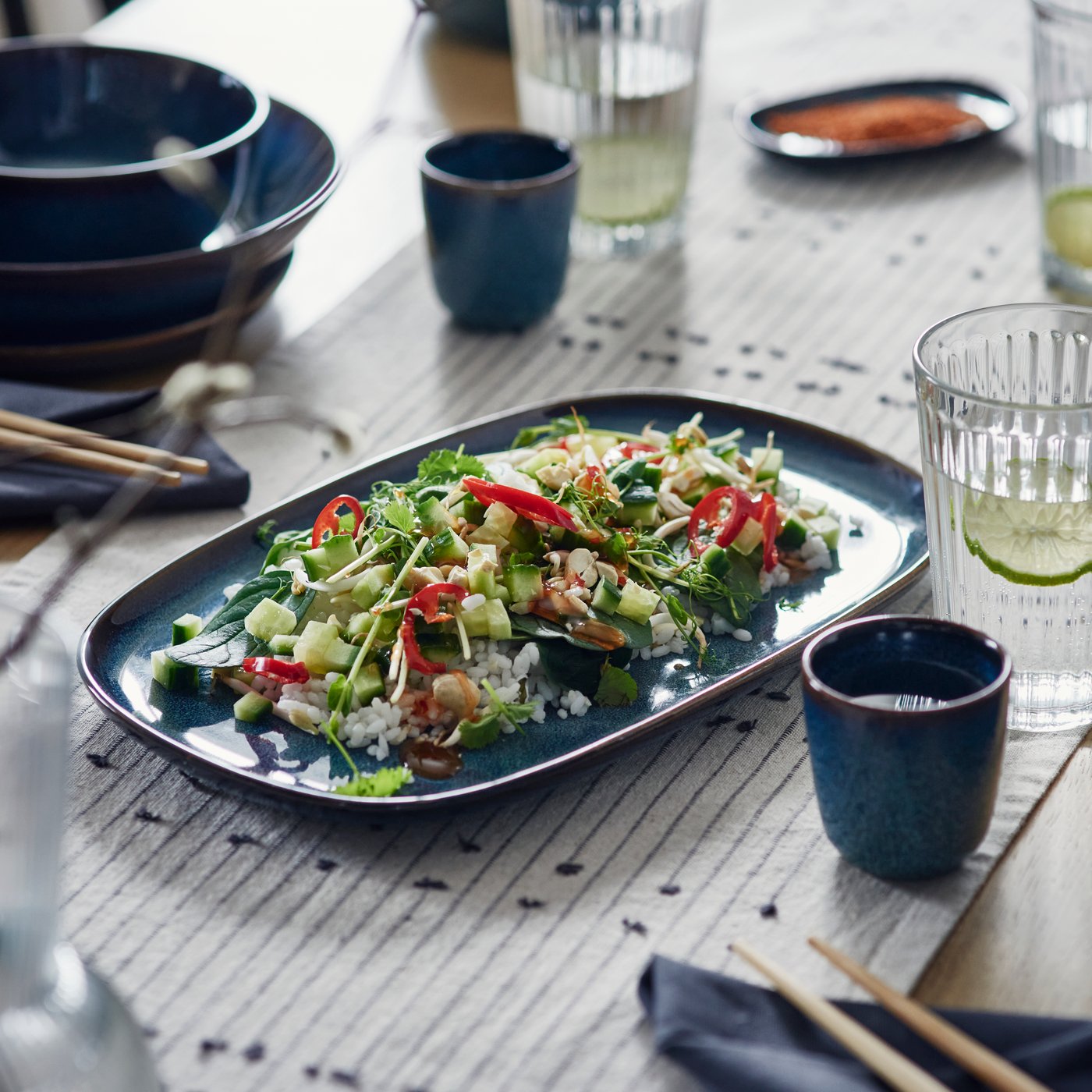 Oválný talíř GLADELIG v modré barvě, na němž je naservírovaný čerstvý salát. 