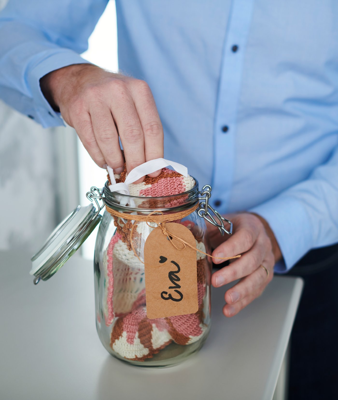 En person i en blå skjorte lægger ting ned i en gennemsigtig krukke med et bånd om, hvor der står et navn på.