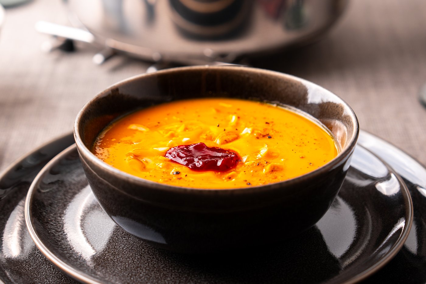 Eine Kürbissuppe, angerichtet in einer schwarzen Schale und einem schwarzen Teller.