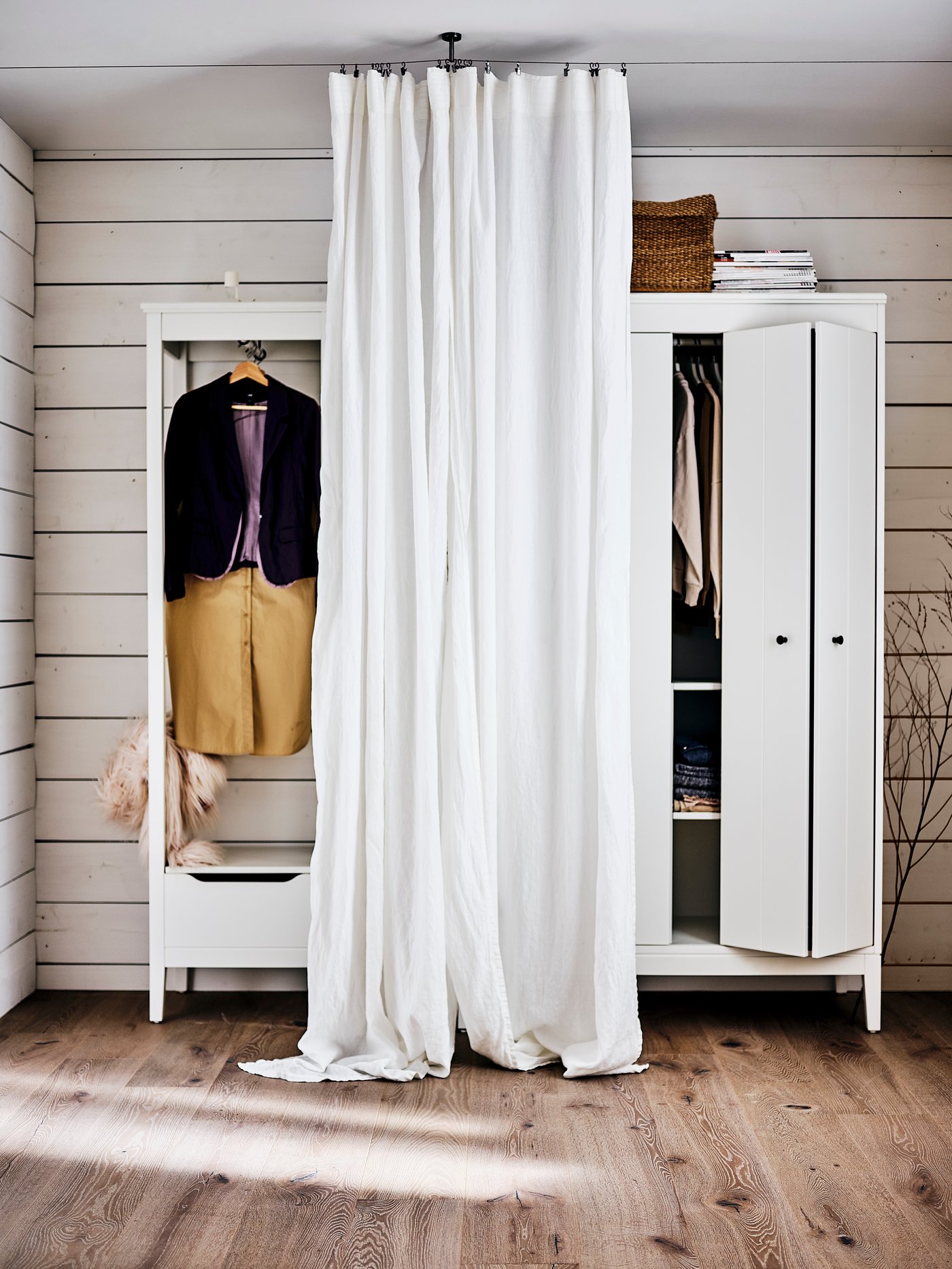 A white IDANÄS open wardrobe and a white IDANÄS wardrobe side by side with a DYTÅG curtain hanging in front of them.