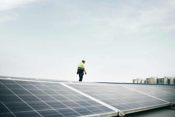 A person wearing helmet and protective clothing is standing on a roof top with solar panels.