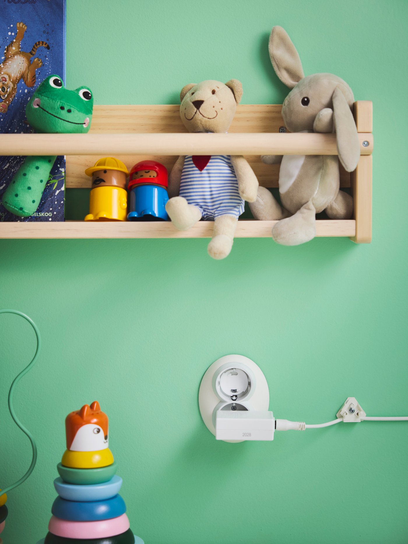 Close-up of FLISAT wall storage full of soft toys such as FABLER BJÖRN and DVÄRGHARE. PATRULL safety plug in socket below.
