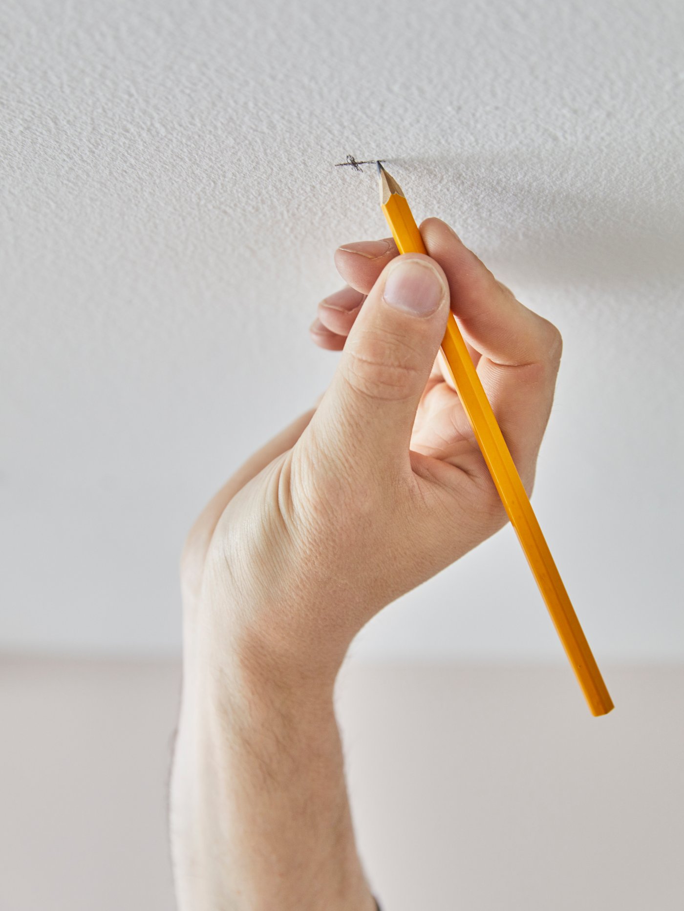 La main d’une personne qui marque un emplacement au plafond dans le but d’y percer un trou pour fixer un rail de rideau VIDGA.