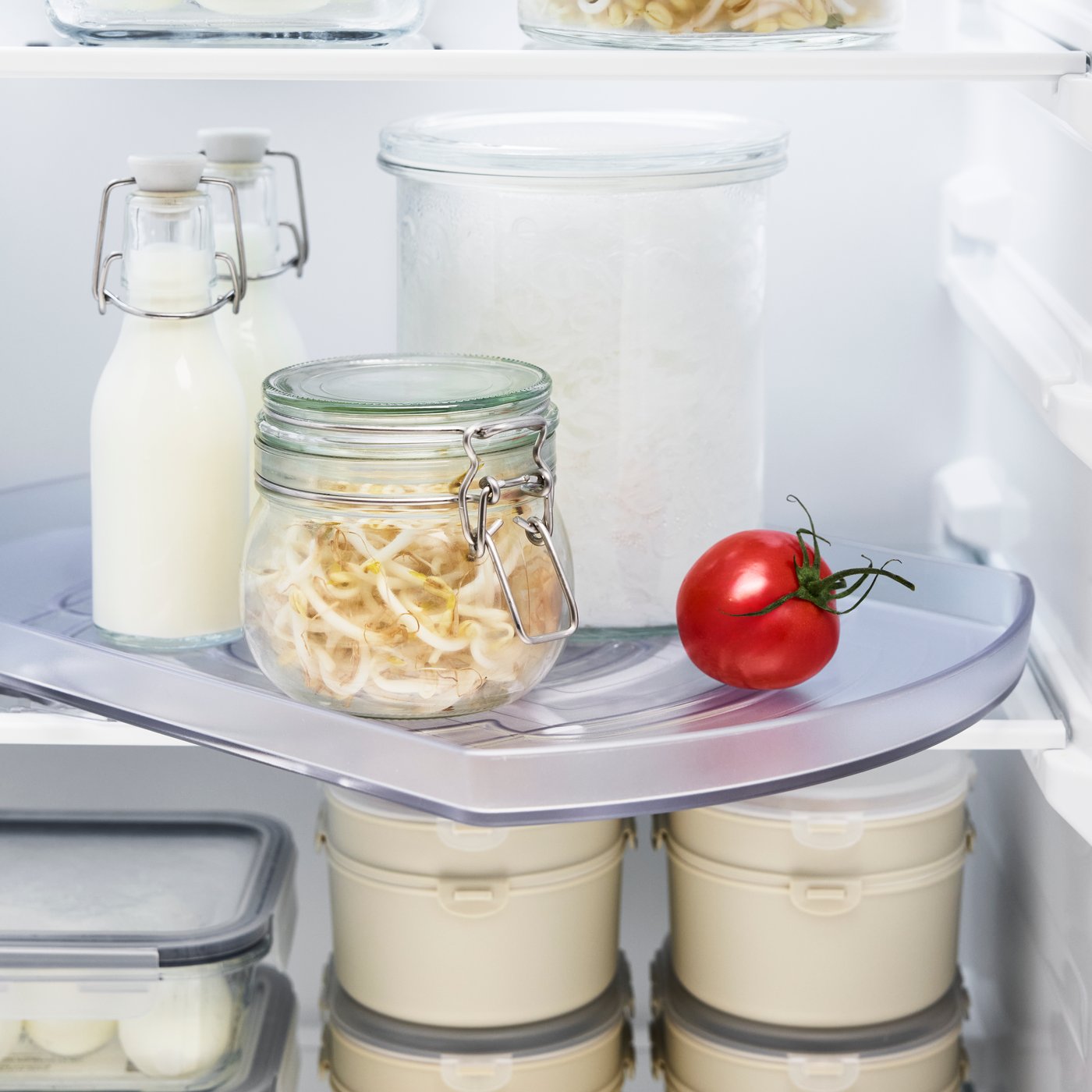 תקריב של מגש מסתובב SNURRAD שמכיל צנצנת עם שאריות, בקבוקי חלב ועגבניות טריות.