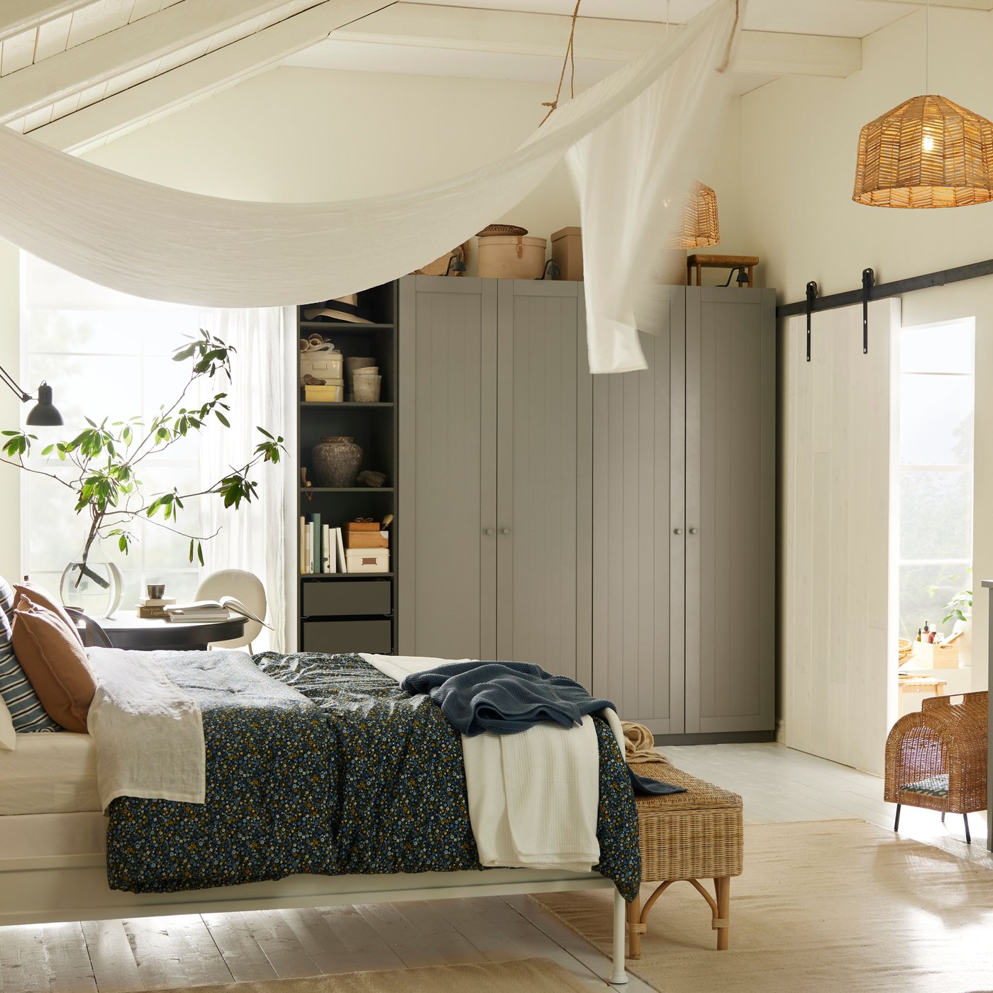 A STJÄRNÖ bed in a bright white bedroom in front of a dark grey/grey PAX/GULLABERG wardrobe combination and a black table.