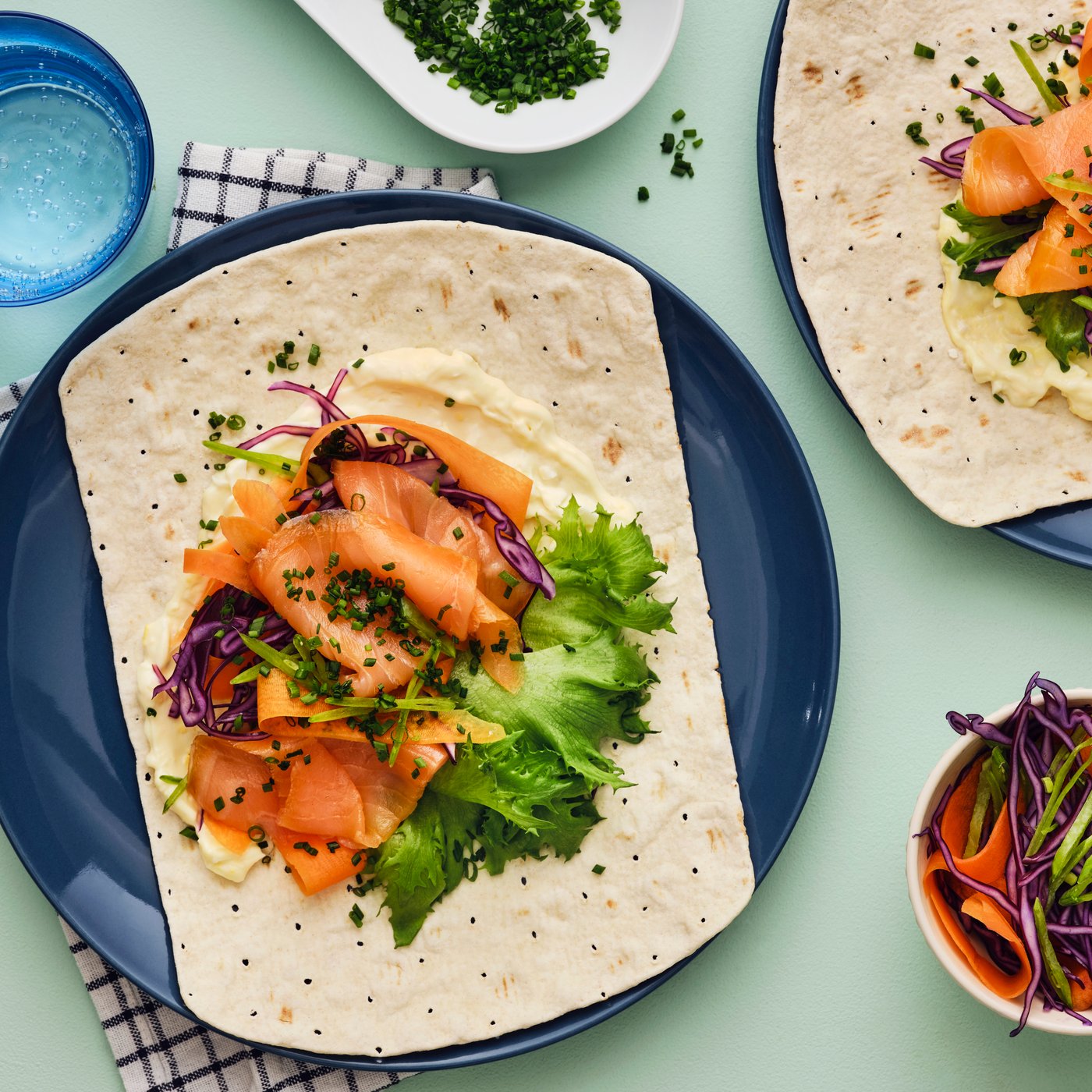 SJÖRAPPORT 셰라포르트 냉훈 연어, 양상추, 자색 양배추를 곁들인 부드럽고 얇은 GRÄDDAT 그레다트 플랫브레드를 고명과 함께 담아 테이블 위에 올려놓은 모습.