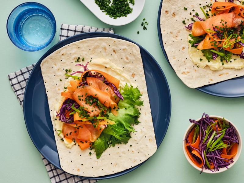 GRÄDDAT mykt tynnbrød med SJÖRAPPORT kaldrøkt laks, bladsalat og rødkål, servert på et bord med ekstra garnityr.