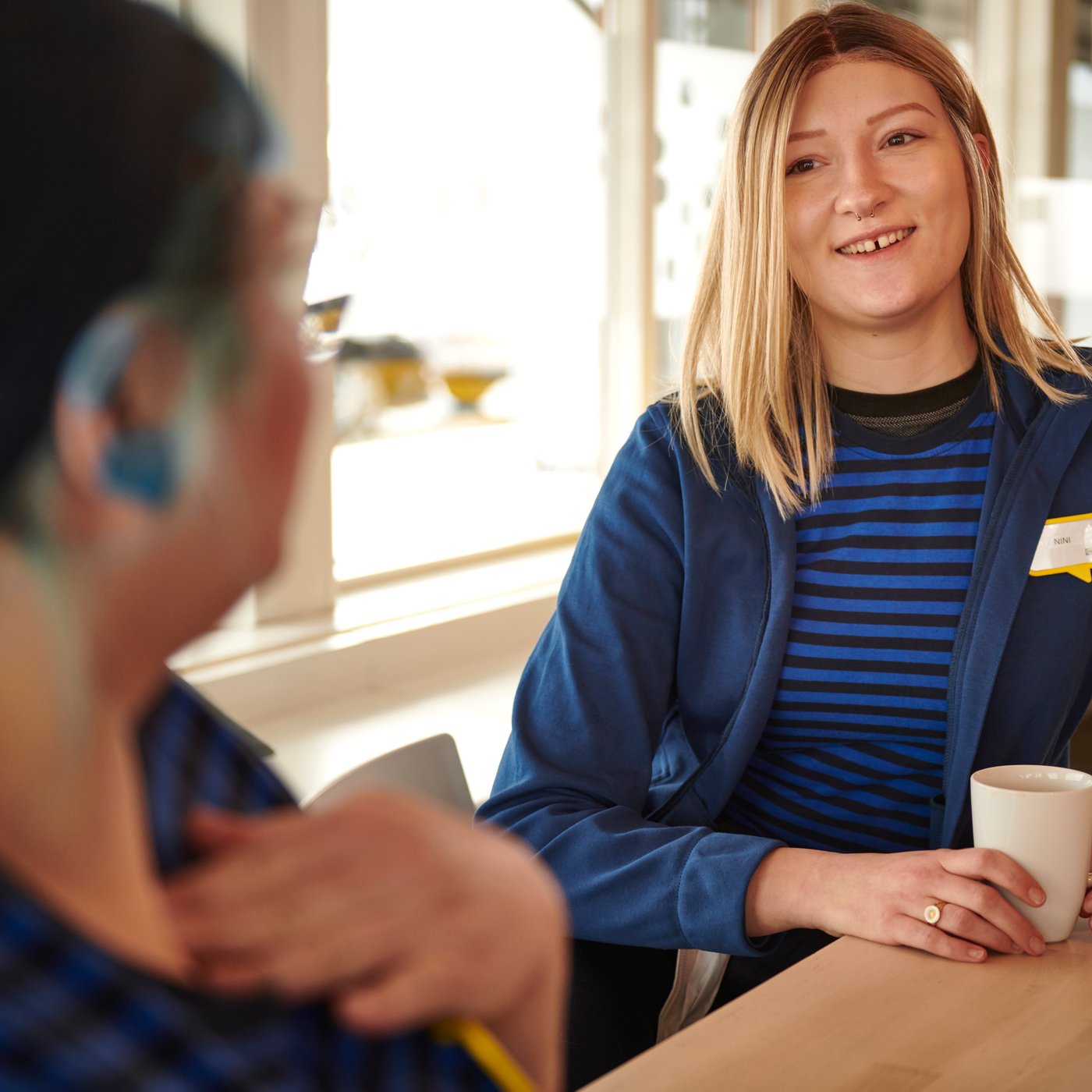 Kaksi IKEA-työasuihin pukeutunutta IKEA-työntekijää kahvilla henkilöstöravintolassa.