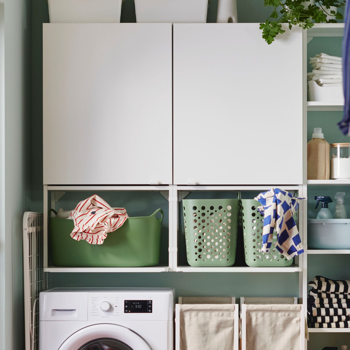 Two side-by-side white ENHET wall shelf frames with deep shelves hold laundry baskets over a washing machine, under cabinets.