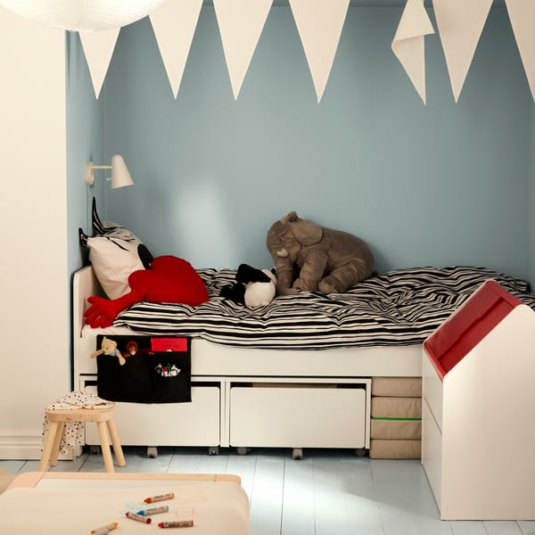 A SLÄKT children’s bed in a niche of the room with blue walls, storage boxes under the bed and NATTHÄGER bedding.