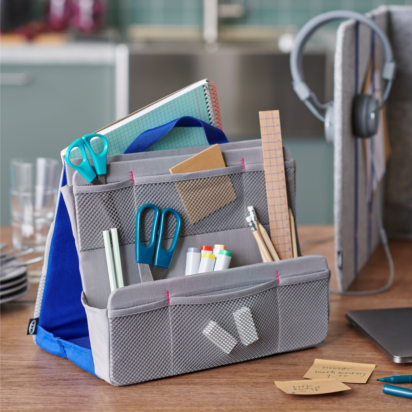 An IKEA ÖVNING desk organiser in grey with various pens and papers on a brown dining table.