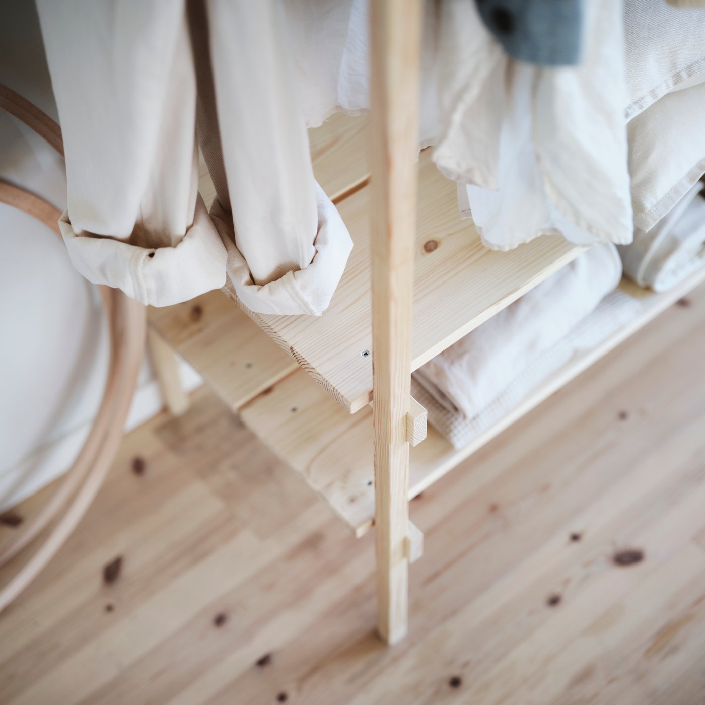 KRONÖREN open wardrobe in pine next to a bed with folded clothes and storage boxes in a compact, tidy room.