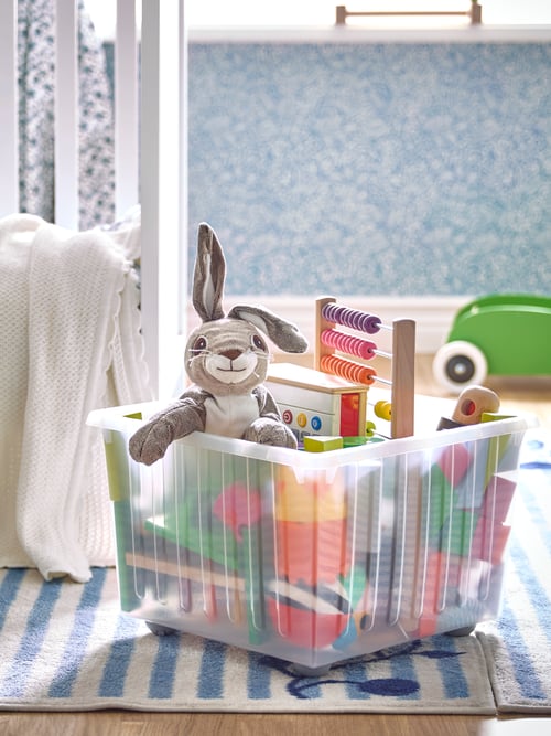 A VESSLA storage box holding children’s toys and a VANDRING hare on a blue and white GULSPARV rug.