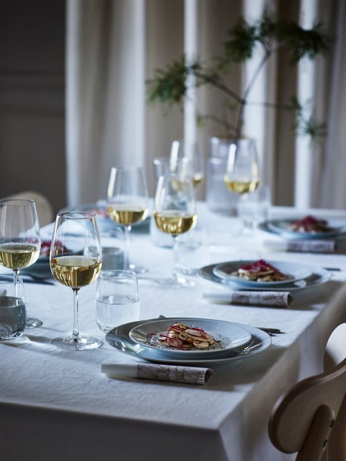 A softly lit table set with a lace-white GULLMAJ tablecloth, white IKEA 365+ plates, and STORSINT wine glasses.