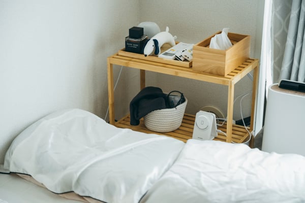白い枕が2つ並び、ベッドサイドに木目調のラックが置かれている。