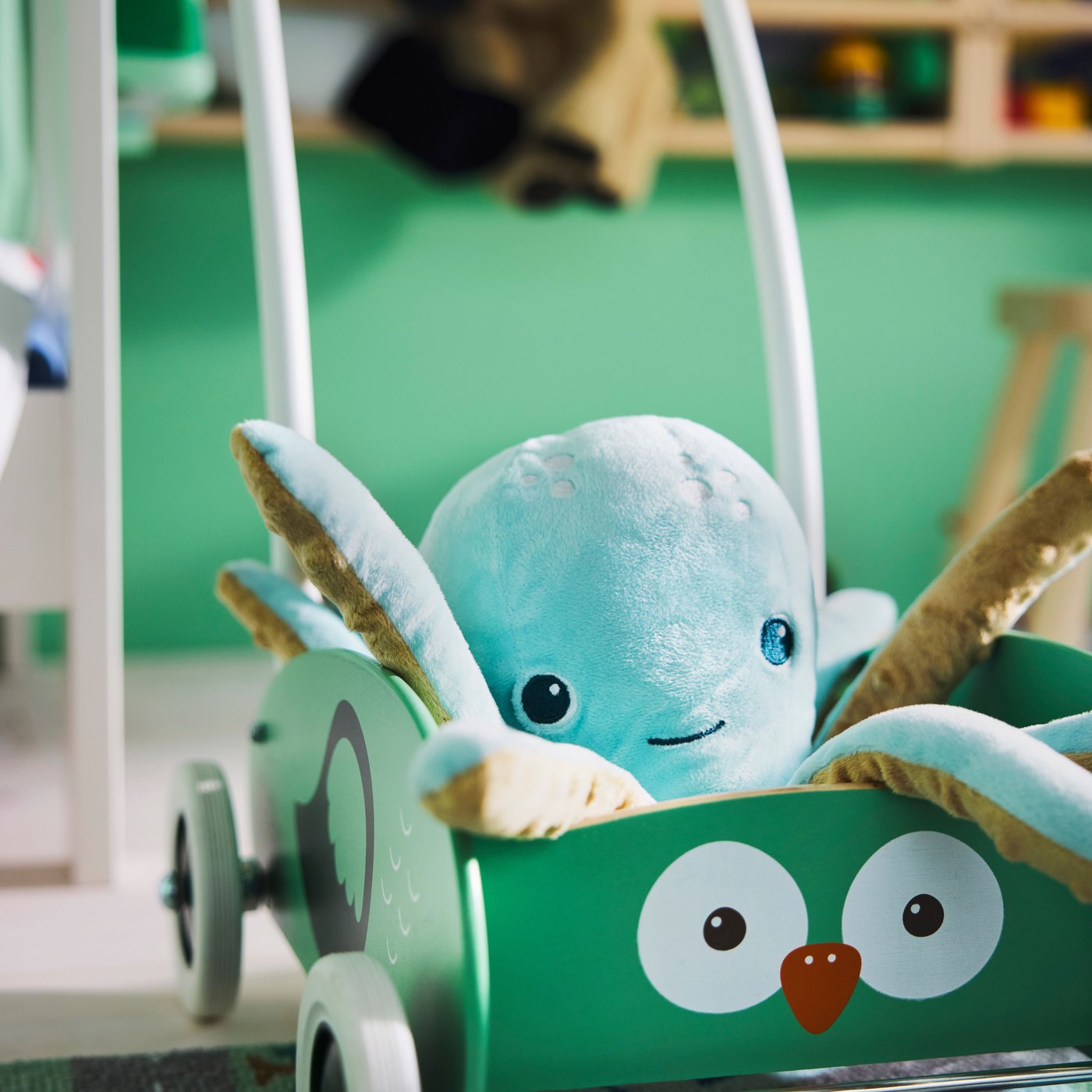 Gros plan sur le trotteur UPPSTÅ pour tout-petits avec une peluche pieuvre turquoise clair à l'intérieur et un tapis vert vif en arrière-plan.