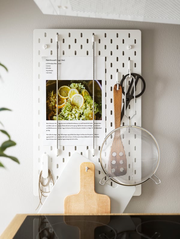 White pegboards on the wall arranged as a menu board, a coffee machine, white cups and plates, clear glasses.