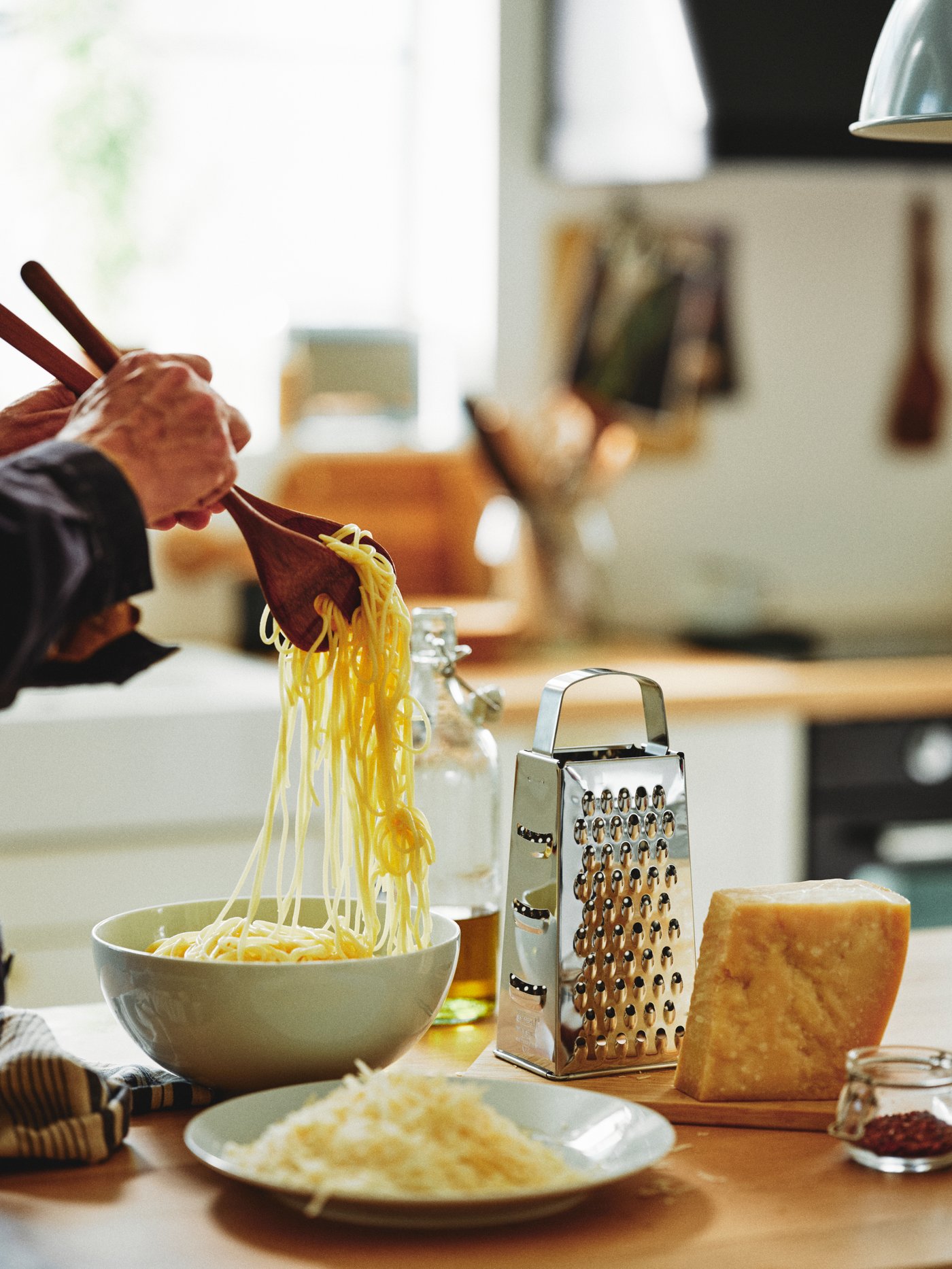 Una persona en una cocina sirviendo la comida junto a un rallador IDEALISK gris y utilizando un juego de 2 utensilios para servir GRÖNSAKER en beige.