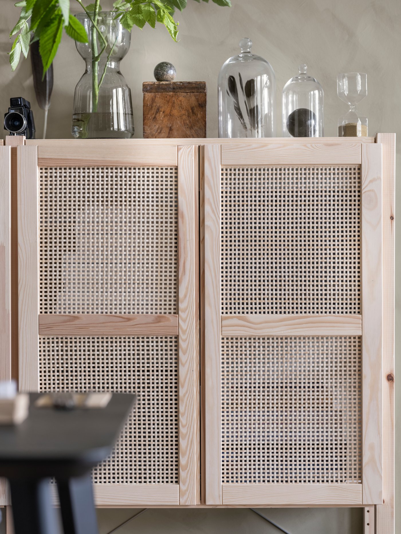 Detalle de un espacio de trabajo moderno compuesto por un armario con una puerta beige de tejido de bambú reemplazable y estructura de pino macizo, con jarrones encima.