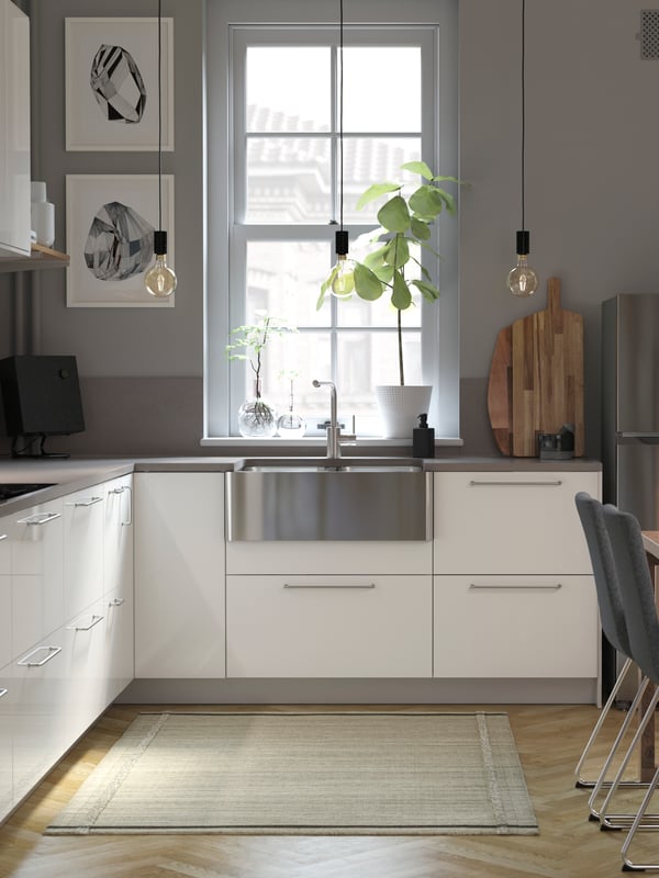 Une cuisine lumineuse avec des façades de tiroir en blanc brillant, des murs gris, une table en bois et un évier en inox.