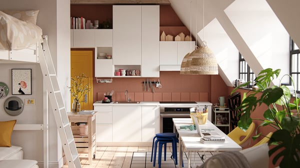 A studio apartment with large industrial-style windows, dark terracotta-coloured walls and white VALLSTENA kitchen fronts.