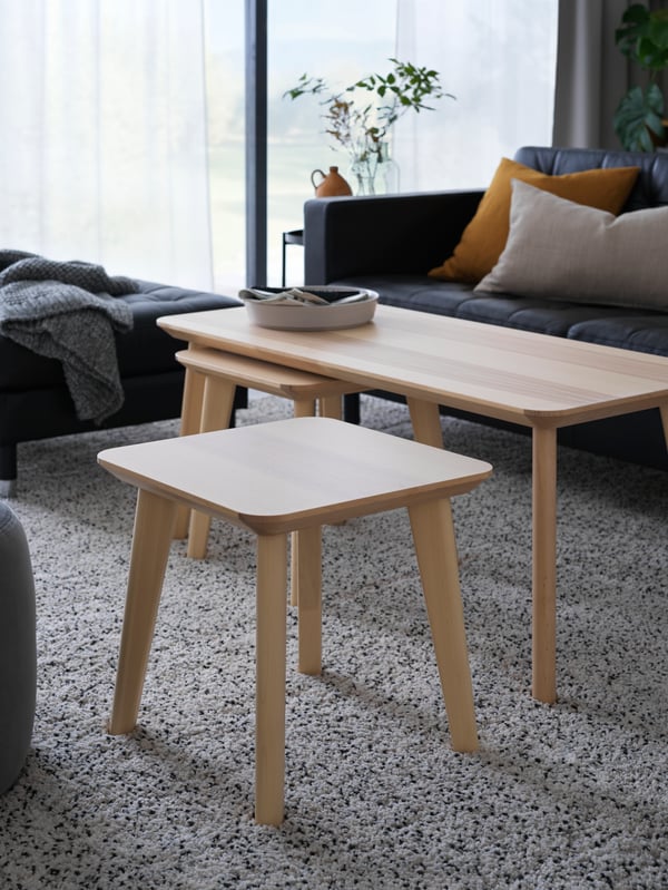 Living room with side table, coffee table, three-seat sofa, serving plate, cushion covers, throw, high pile rug, plant pot.