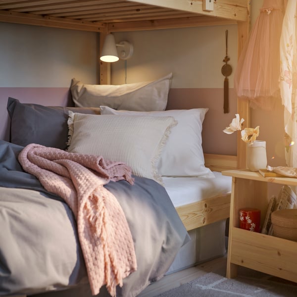 The bottom bunk of a MYDAL pine bunk bed covered with grey ÄNGSLILJA bed linen and a pink HORNMAL throw.