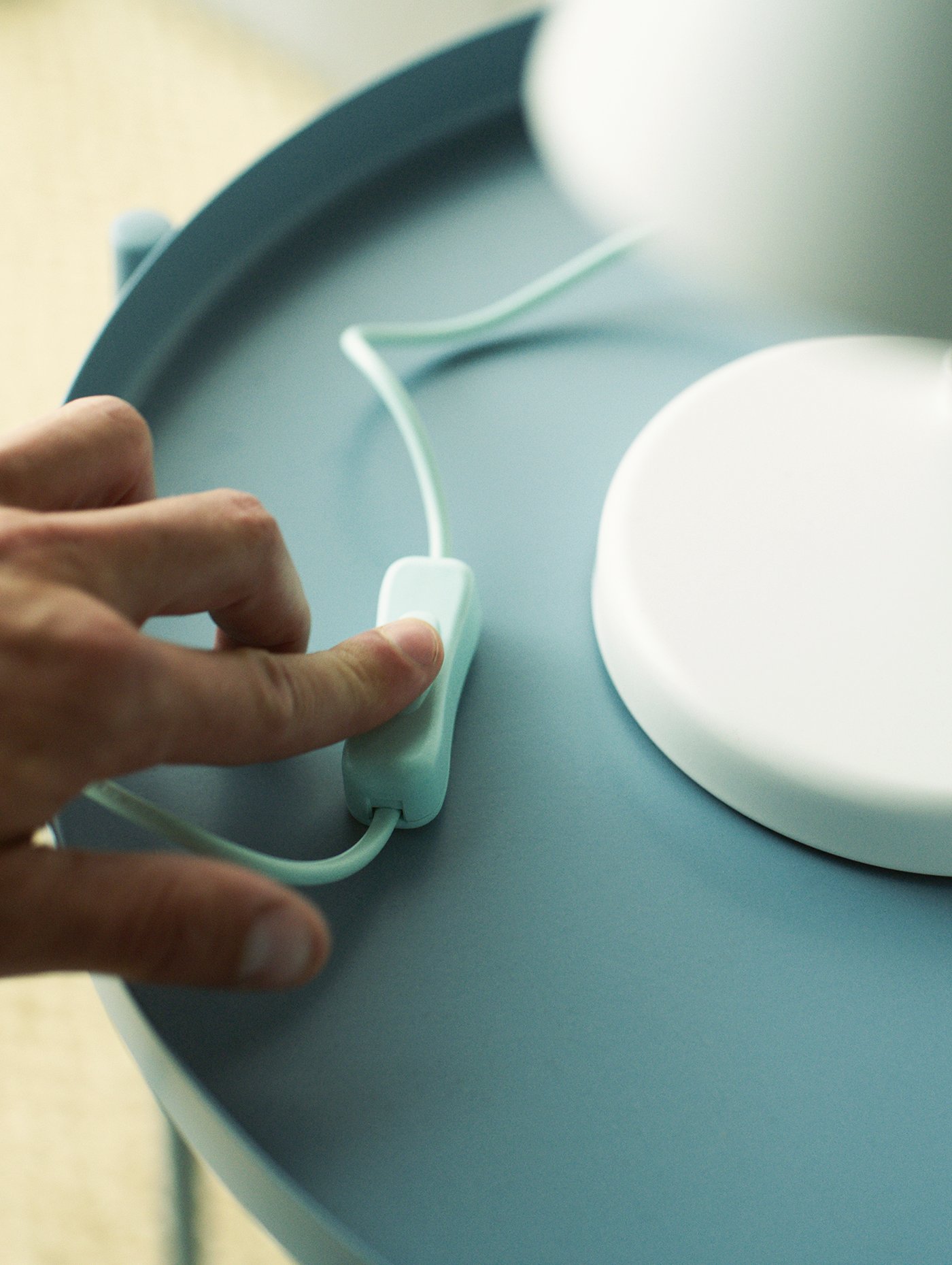 أصابع شخص على مفتاح مصباح عمل FUBBLA LED موضوع على سطح طاولة أزرق.