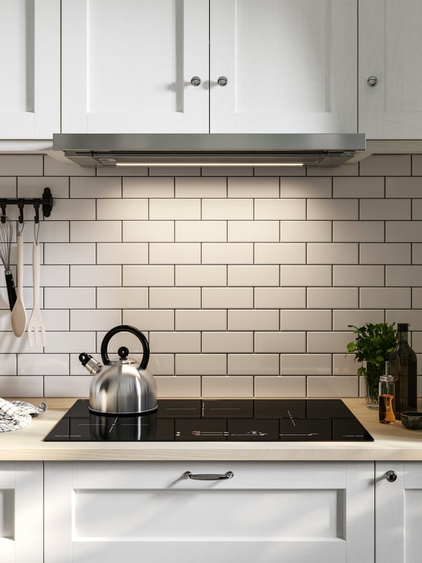 A kettle is placed on a black MATMÄSSIG induction hob in a kitchen with base and wall cabinets with white ENKÖPING fronts.
