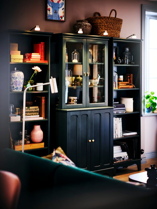 Living room with a cabinet with glass doors, blue bookcases, LED cabinet lighting, vases, a basket, books, personal items.