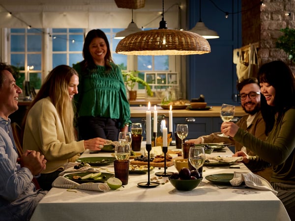 Mensen zitten rond een eettafel voor een maaltijd van kaas en vers fruit, allemaal in een gezellige sfeer met kaarsen.