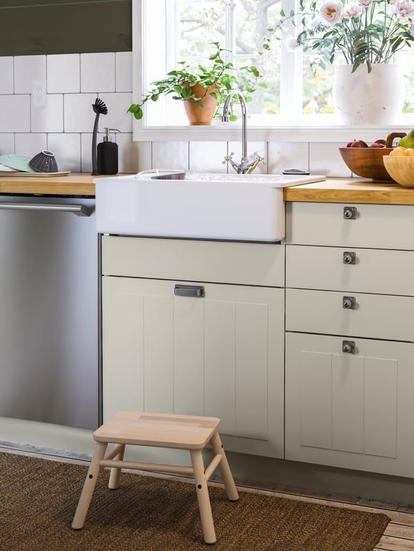 A step stool against the kitchen counter and sink, bowls, washing-up accessories, plants by the window.