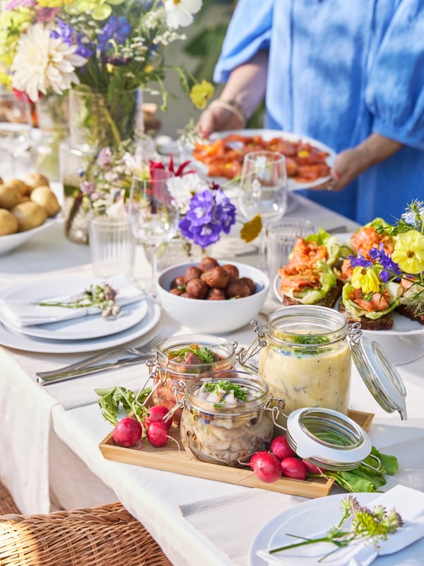 En person står och tar mat vid ett dukat midsommarbord.