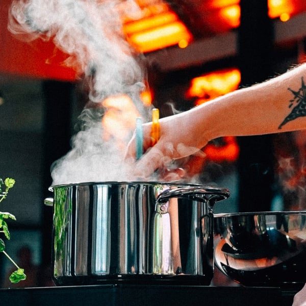 Una mano immerge delle bacchette all'interno di una pentola in acciaio inox dove usce una nuvola di vapore: il momento esatto in cui profumi, sapori e curiosità si incontrano in cucina.