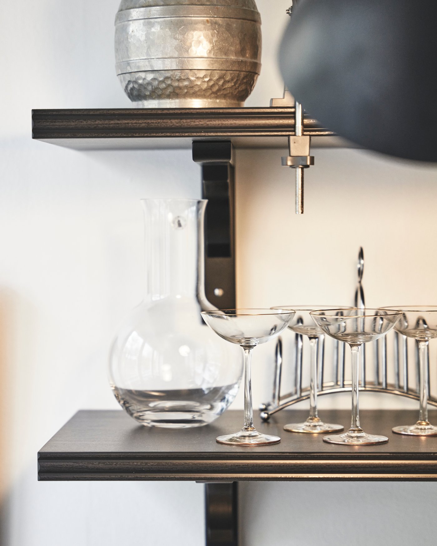 Svarta hyllor mot en vit vägg, där glas står uppradade.