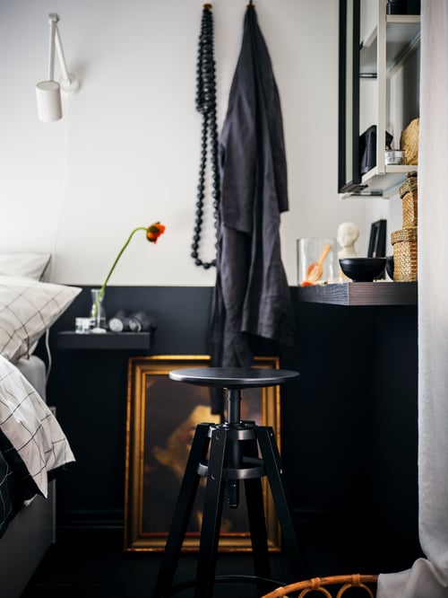 A bedside area with a black-brown LACK shelf acting as bedside table, a black DALFRED bar stool and an ENHET mirror cabinet.