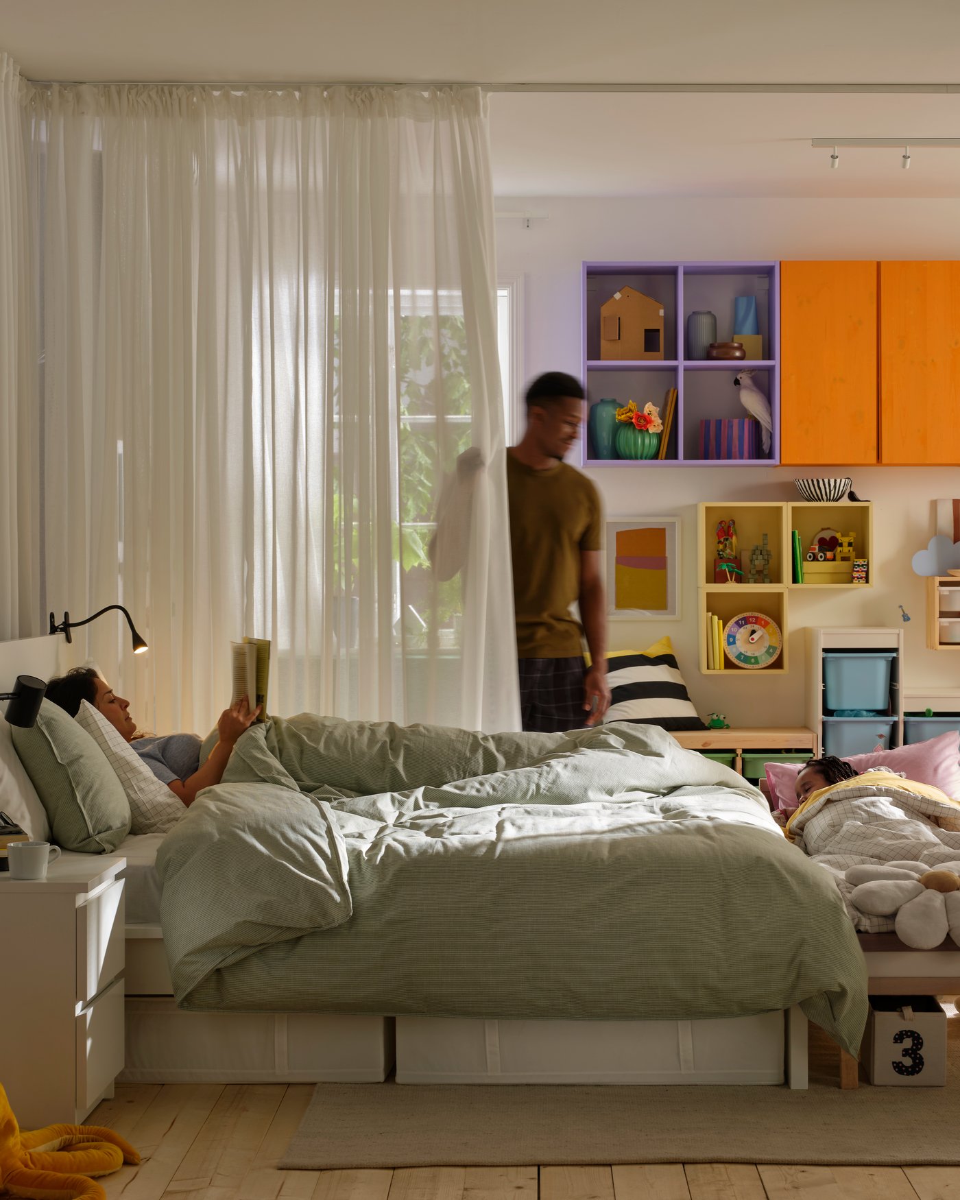 A person pulls the curtains that hang from VIDGA single track rails near a bed that another person is lying in.