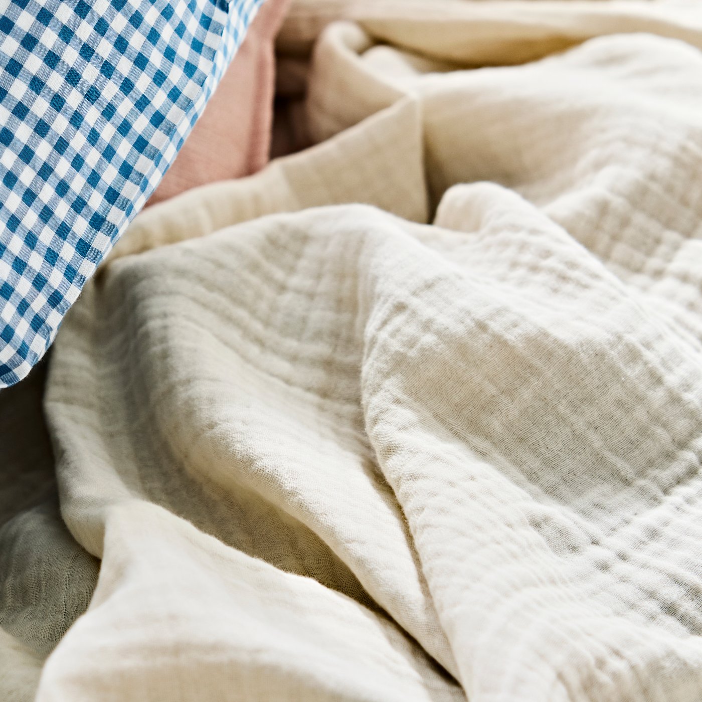 Off-white VALLKRASSING cotton muslin throw with a soft, crinkled texture draped casually over bedding.