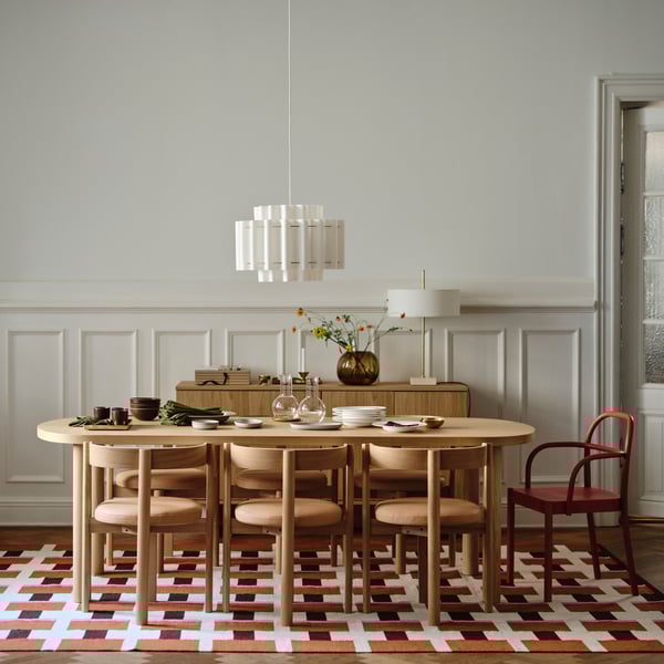 A room with a dining set on a patterned rug. A pendant lamp hangs above and there’s a sideboard with a table lamp behind.