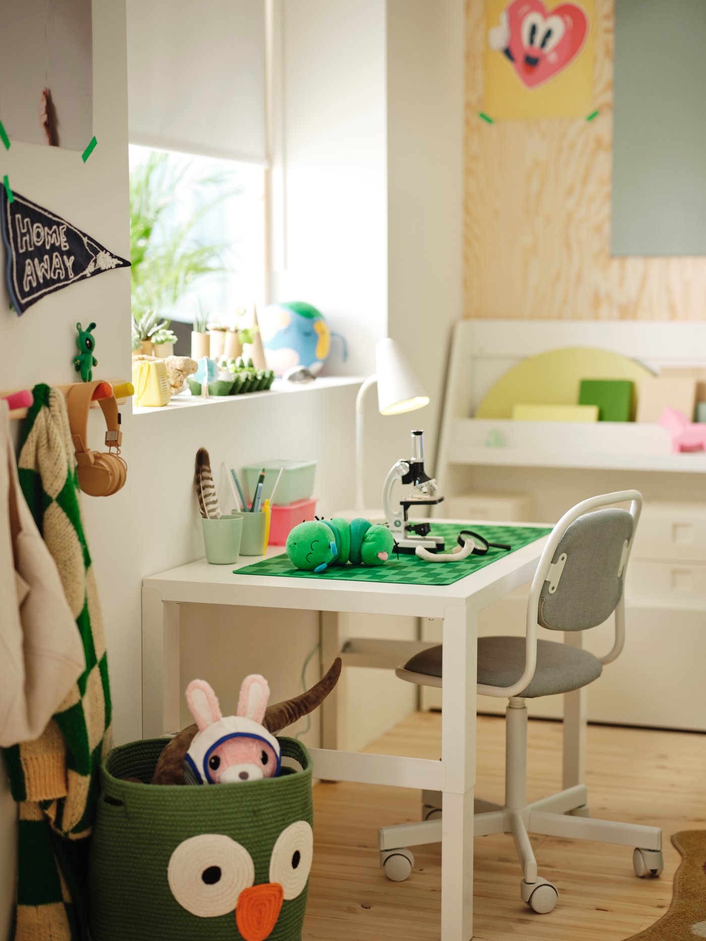 A PÅHL desk with a chair faces out of a window lined with decorations. Next to the desk is a UPPSTÅ storage bag with toys.