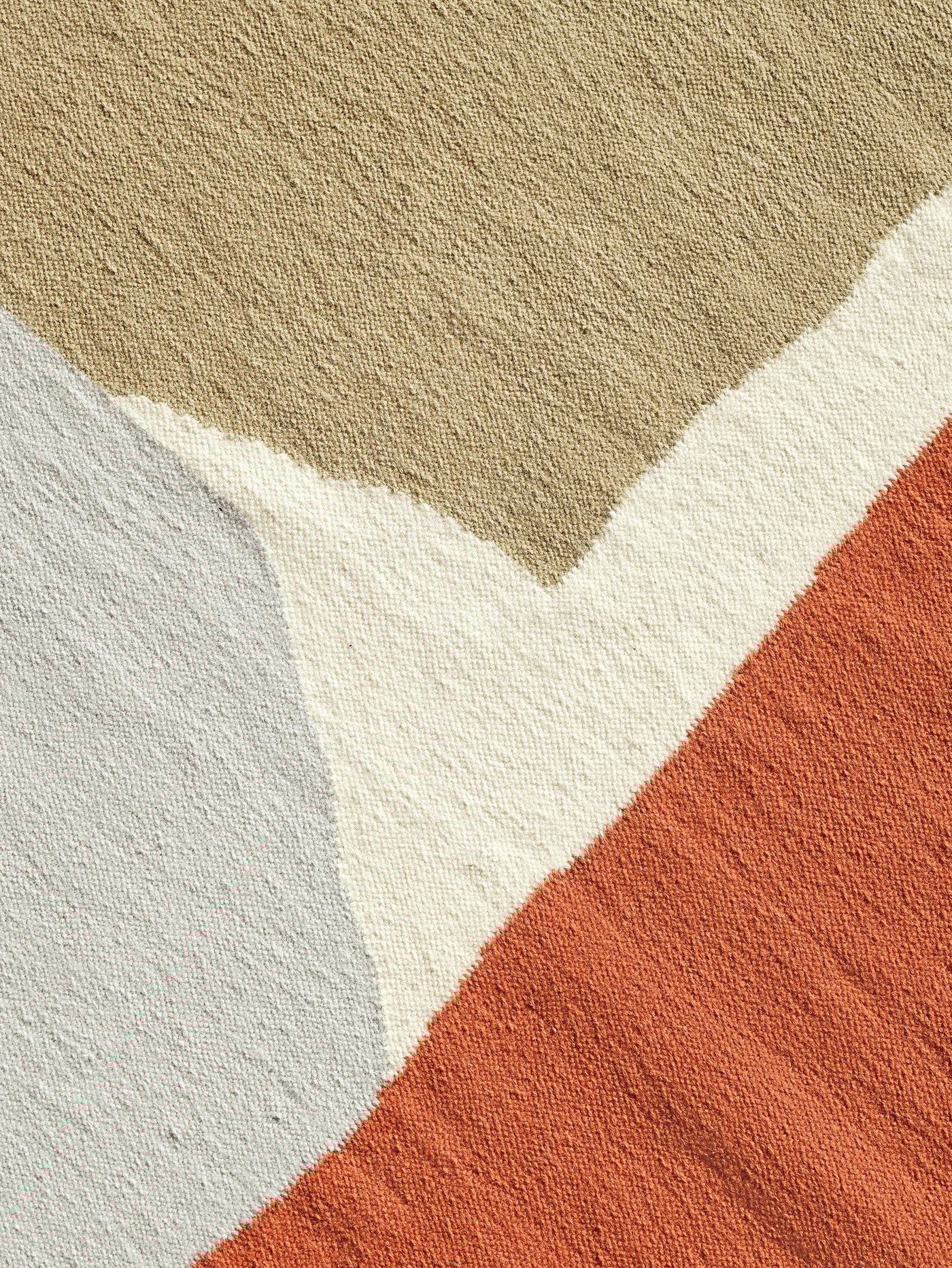 Details of the beige, white, orange and grey patterns of abstract shapes on the TVINGSTRUP handmade rug.